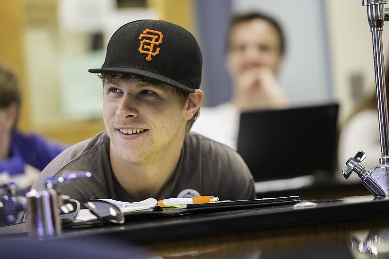 Student in baseball cap smiles while seated at science lab 选项卡le